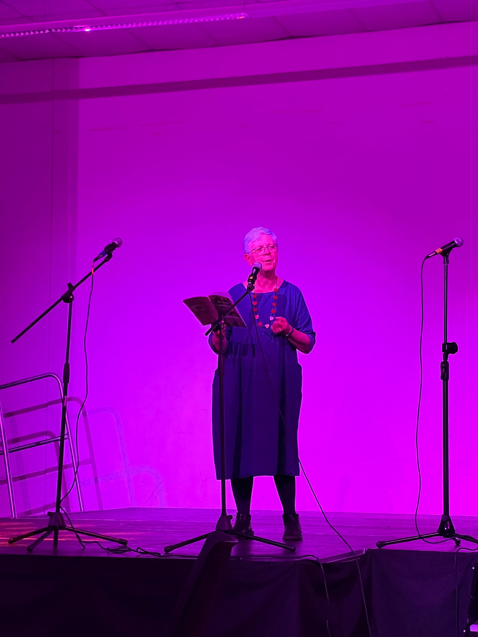 Poet performing onstage under soft purple lighting, captured in a moment of quiet reflection and spoken word expression.