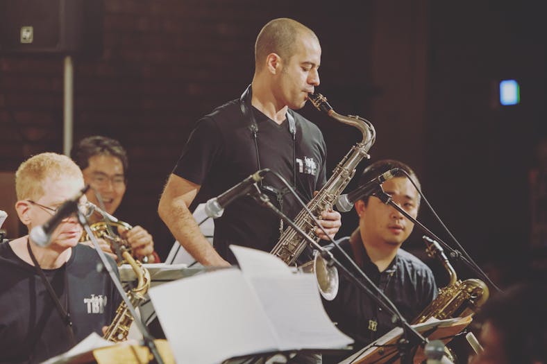 Male saxophonist performing live with an orchestra, captured mid-performance in a moment of musical expression.